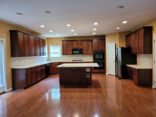 Kitchen with dark wood cabinets, center island, recessed ceiling lights, and hardwood floors.