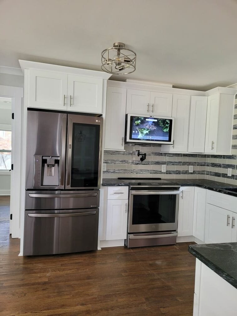 Finished kitchen sink area with white cabinets, dark counters, and tile backsplash