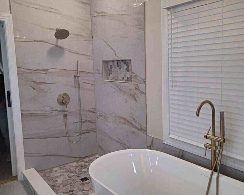 Finished bathroom remodel with freestanding tub, marble-look tile, and brass fixtures